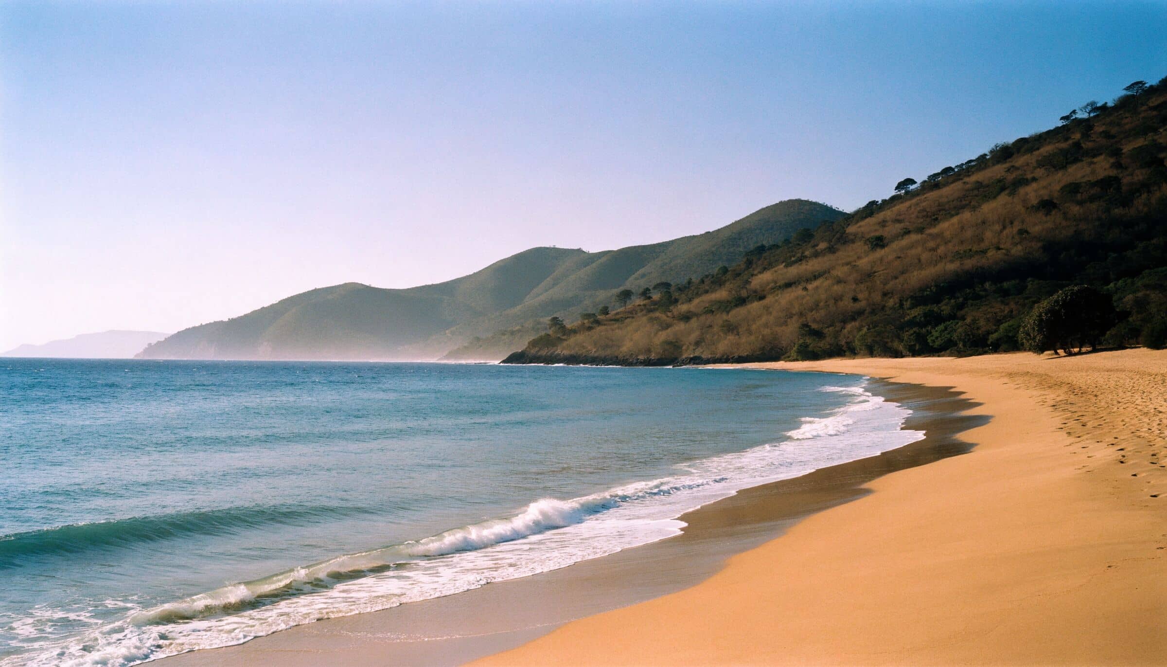 Une longue plage dorée du Pacifique nord, entourée de collines de forêt sèche